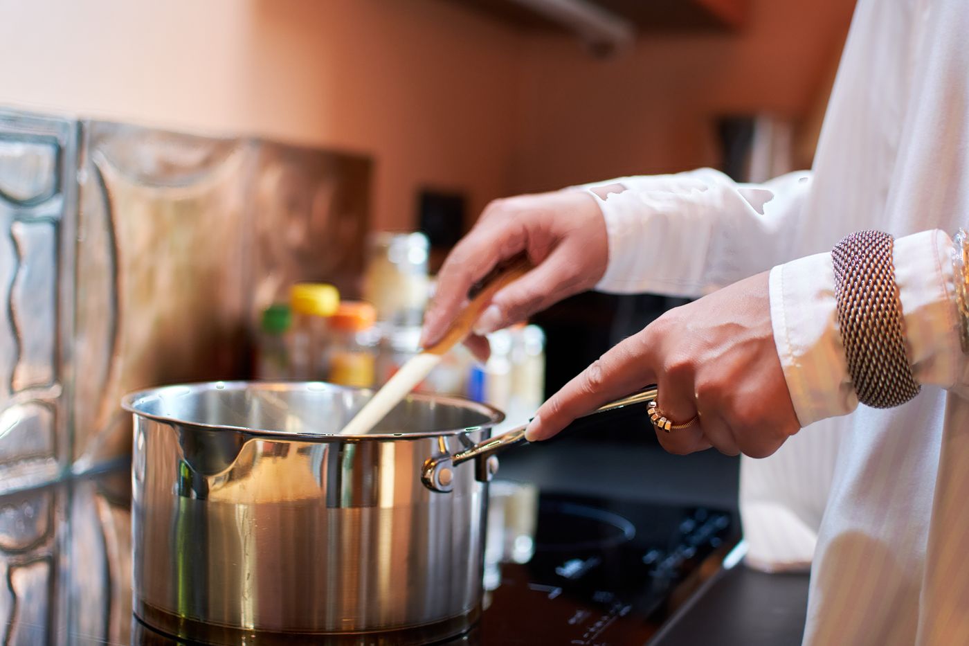 Hands stirring a saucepan with a wooden spoon on the hob, in a kitchen with terracotta walls
