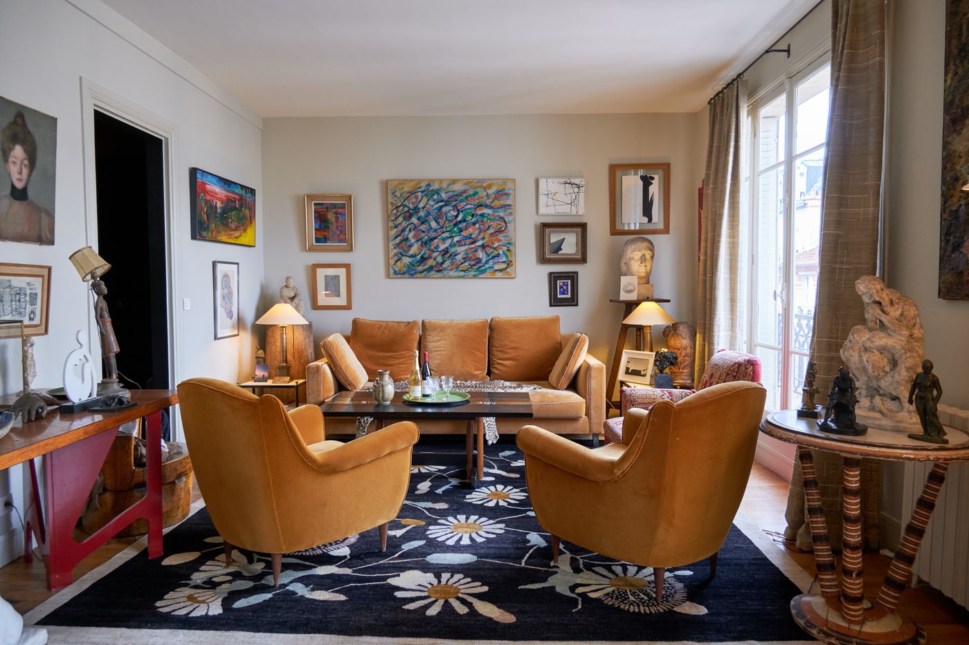 The living room seen from the dining area: two velvet armchairs, a sofa, a red-legged console with sculptures and paintings on every wall